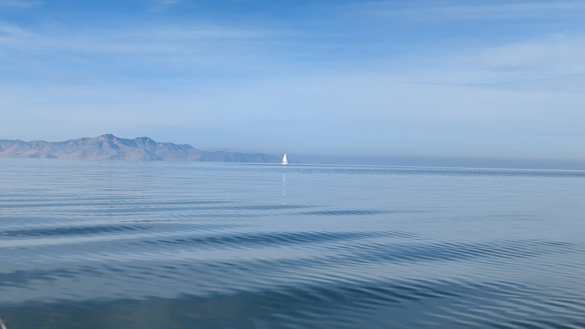 A sailboat in the distance sailing off the coast of some mountains.